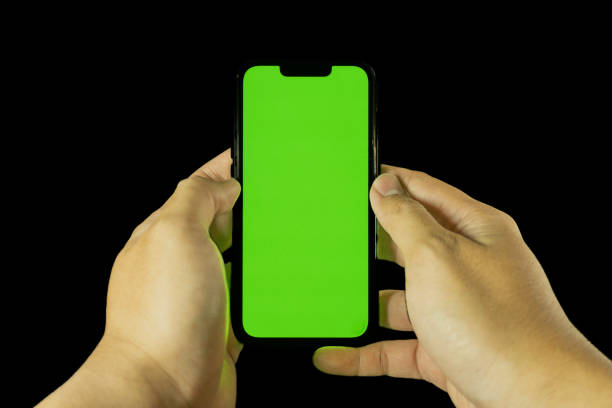 istock Asian man's hand holding iphone smartphone with blank green screen on solid black background 2180631438