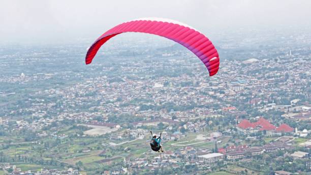 istock Paraglider pilot  flying high in blue sky and village scenery 2180642959