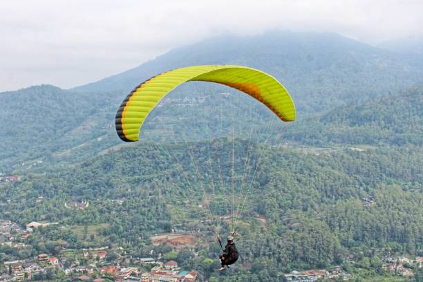 istock Paraglider pilot flying high in blue sky with village and mountain view 2180643006