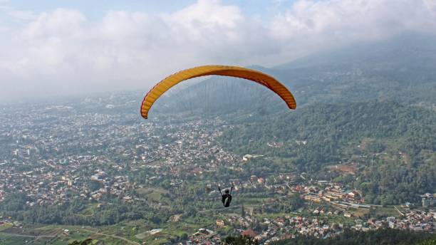 istock Paraglider pilot flying high in blue sky with village and mountain scenery 2180643077
