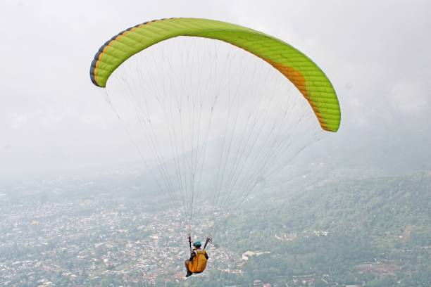 istock Paraglider pilot flying high in blue sky with village and mountain scenery 2180643143