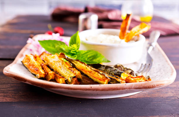 Baked zucchini sticks with herbs on a light plate. Top view