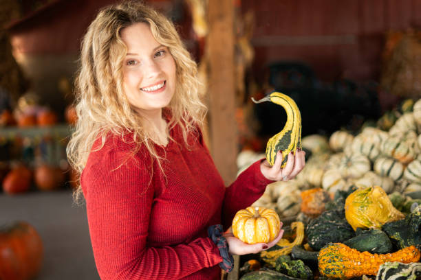Blond smiling woman holds small gourds at a farm stand in Autumn