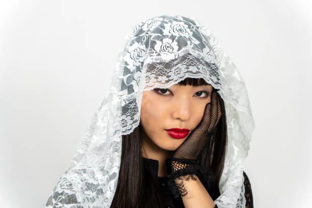 Close up of woman with eyes closed wearing black mourning veil made of delicate lace covering face in studio