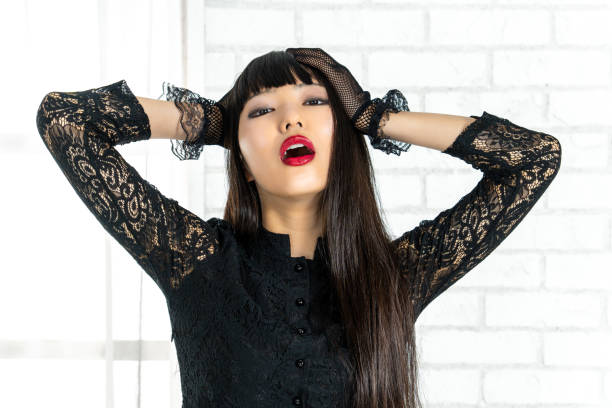 Close-up of a young woman with a serious expression. She looks angrily and disappointedly to the side. Heavy make-up, visible beauty mark and defined red lips. Studio lighting, partial shadow, tight neckline.