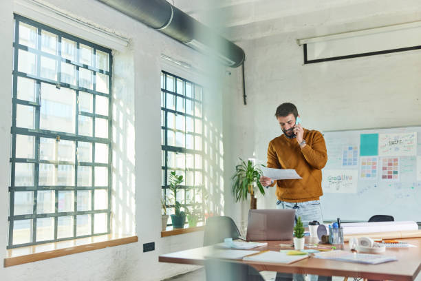istock Happy freelancer reading reports while talking on cell phone at casual office. 2180673952
