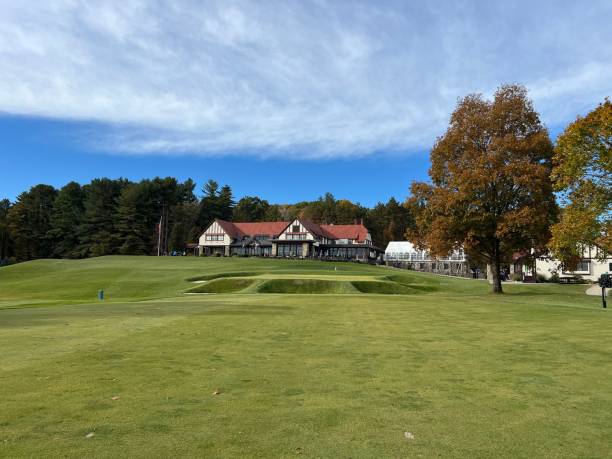 A scenic view of a golf course with a clubhouse in the background, surrounded by trees under a clear blue sky.