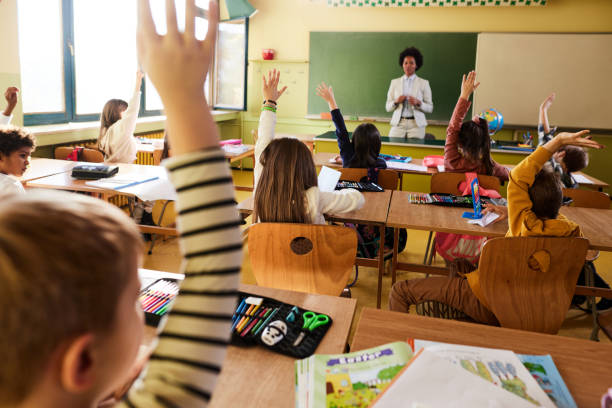 istock Back view of students raising their hands to answer the teacher's question on a class. 2180675029