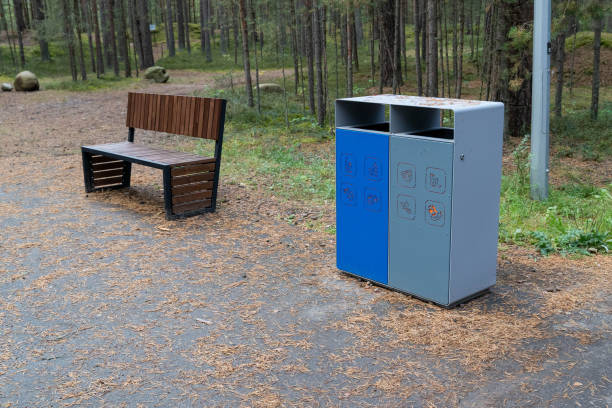 istock Modern trash cans standing on asphalt in park surrounded by forest 2180677819