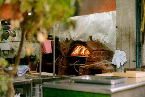 Stock photo showing close-up view of a traditional brick oven for cooking pizzas at an Italian pizzeria restaurant, brick-built wood burning stove with orange flames burning logs.
