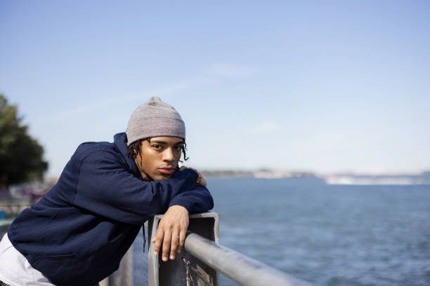 Carefree African American man leaning on a fence at riverbank and looking at camera.