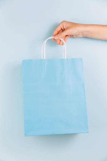 istock Female hand holding blue paper bag isolated on blue background 2180693682
