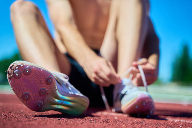 A man is sitting on the ground with his feet up. He is wearing white shoes with spikes on the bottom