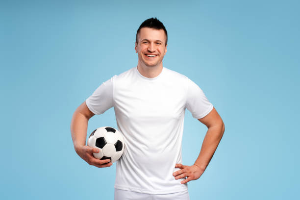 istock Happy soccer player holding a ball smiling at blue background 2180702547