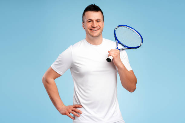 istock Smiling young tennis player holding racket posing on blue background 2180702573