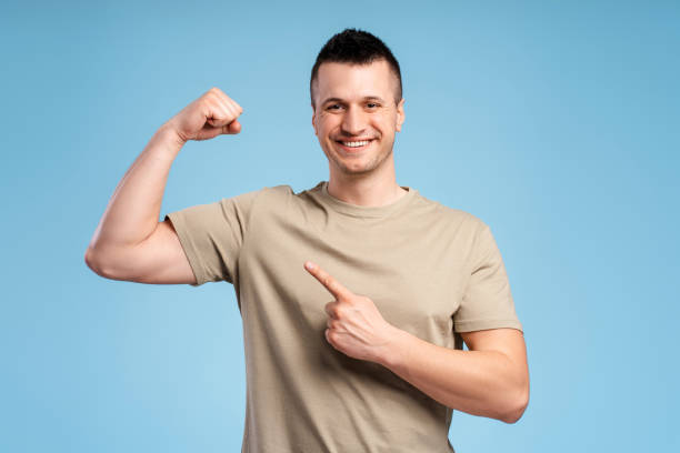 istock Strong, athletic, smiling man in pastel t shirt pointing biceps, showing strength 2180702645