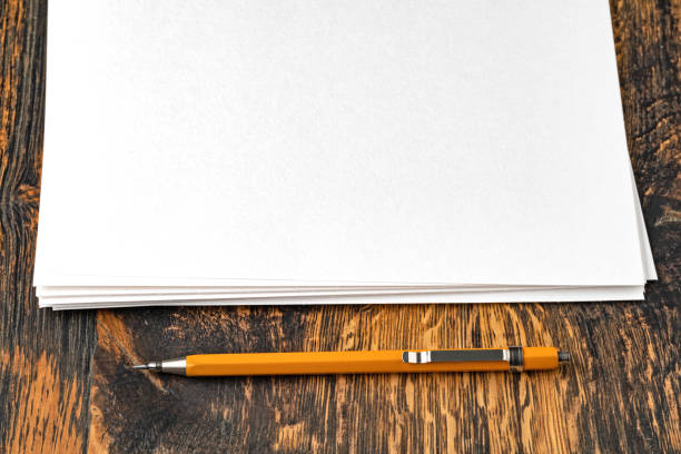 A white ballpoint pen with a brown tip lies next to an open grid notebook with a spiral binding on a bright orange background.