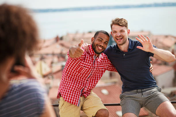 Couple of gay men smiling at a lookout point pointing, with the city in the background. LGBT couple concept