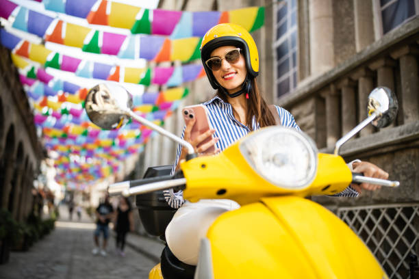 istock Woman sitting on yellow moped and using her phone. 2180714055