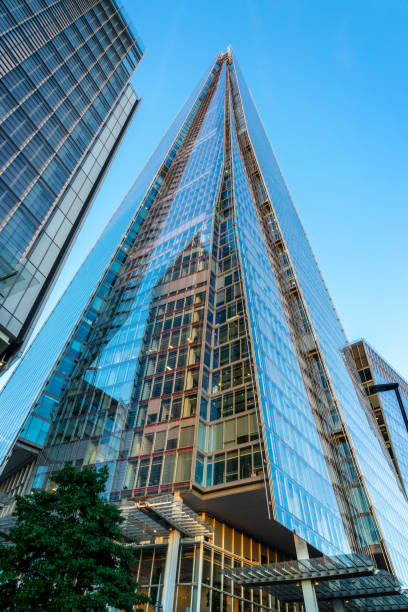 Upward view of The Shard, London’s iconic glass skyscraper, glowing against a dark night sky. The illuminated windows and sharp architectural lines highlight the modern design and towering presence of this landmark building. Photographed from street level, the image captures the dramatic perspective and urban atmosphere.