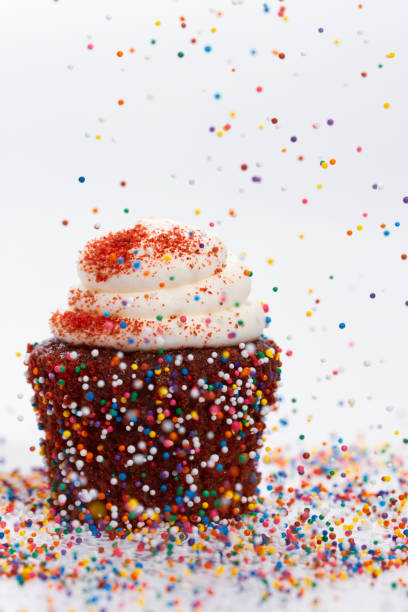 Red velvet cupcake with sprinkles falling on top of it against a white background.