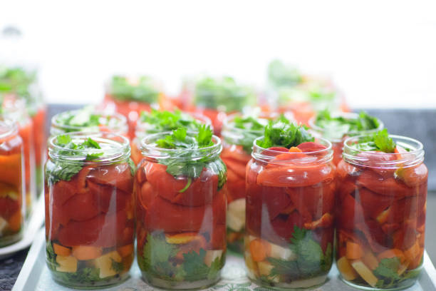 Fresh red peppers, carrots, and celery sliced and prepared for pickling in glass jars. A vibrant scene of homemade food preservation and sustainable living.