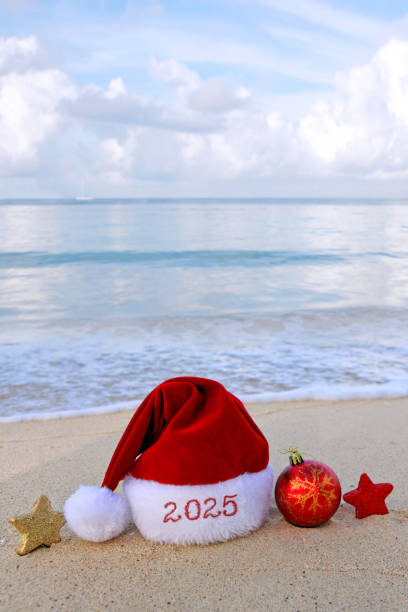 istock New Year 2025 background with Christmas hat and decorations on Caribbean sand. 2180732409