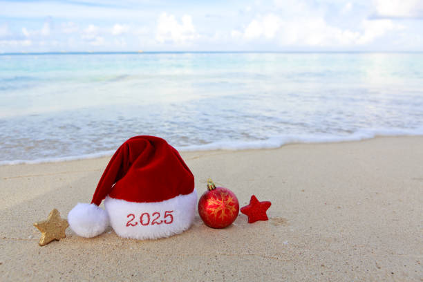 istock New Year 2025 background with Christmas hat and decorations on Caribbean sand. 2180732478