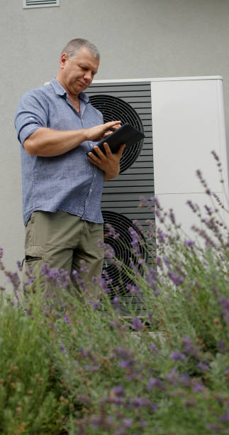 istock A homeowner checks a heat pump unit's settings on a tablet amidst lavender. 2180737032