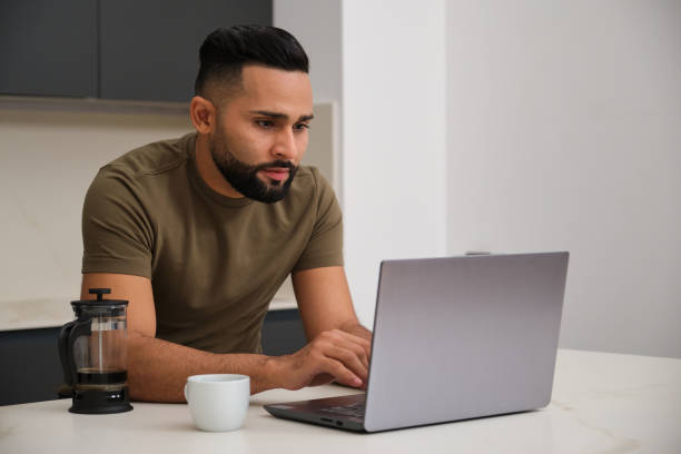 istock Focused young freelancer working from home using laptop in the kitchen 2180750210
