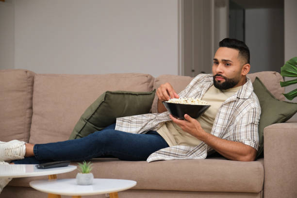 istock Handsome young man relaxing on sofa watching tv and eating popcorn 2180750493