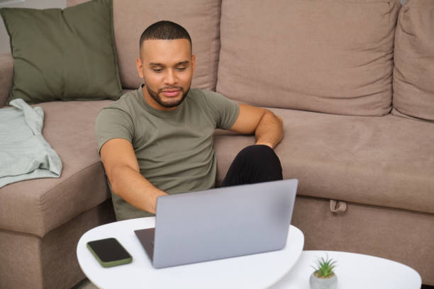 istock Focused young man working from home sitting on the floor using laptop computer 2180750499