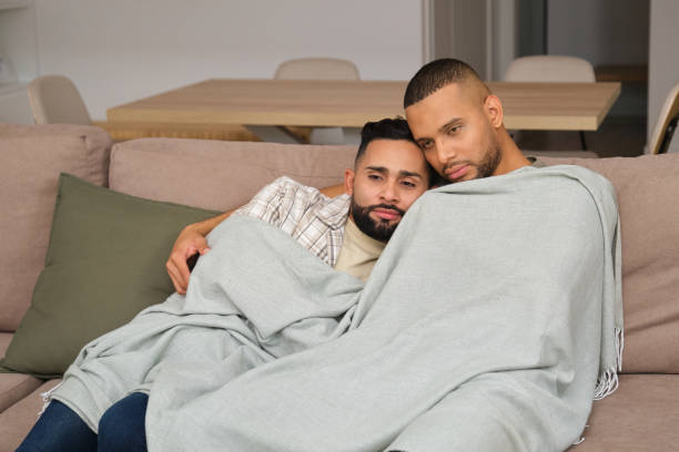 istock Gay couple relaxing on sofa under blanket at home 2180750507