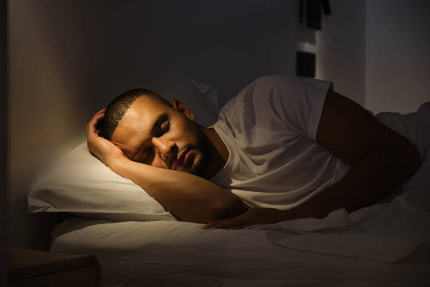 Depressed man lying in bed on a pillow and looking out the window, top view