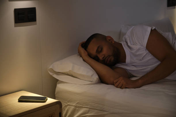 istock Young man sleeping peacefully in bed at night with smartphone on nightstand 2180750570