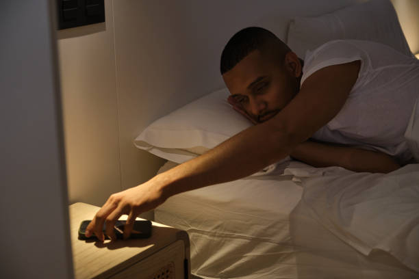 istock Tired man reaching for alarm clock in bed 2180750578