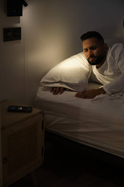 istock Young man having trouble sleeping looking at phone on bedside table 2180750594