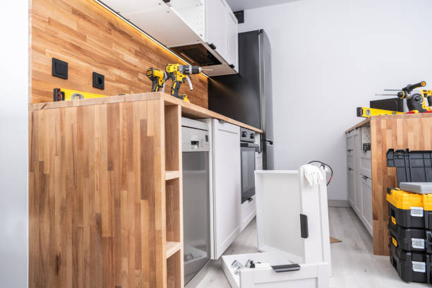 Renovation work is underway in a modern kitchen featuring sleek cabinets, tools on the counter, and light wood surfaces. The space is bright and organized for efficiency.