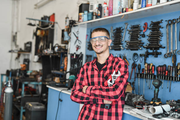 istock Smiling Joyful Young Mechanic Posing for Camera in His Small Car Repair Workshop Holding Tools 2180762877