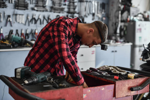 istock Concentrated Young Adult Arranging Tools in Big Tool Box in Small Mechanic Workshop 2180763493