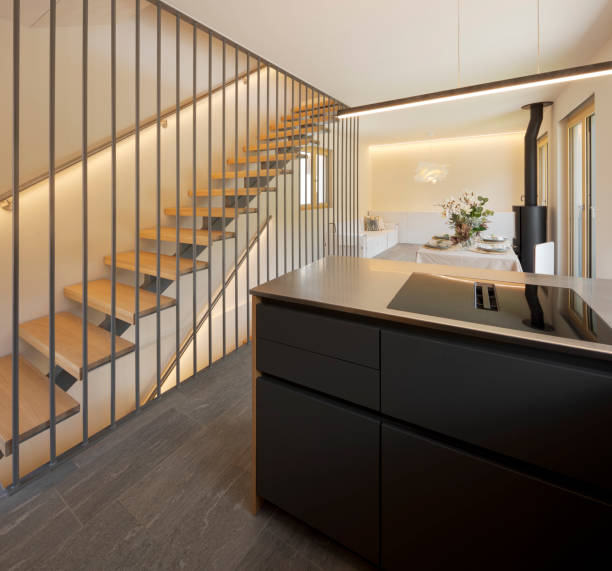istock Open space with a kitchen island, a table and at the back the sofa and the stove. On the left a modern staircase in wood and metal. 2180767046