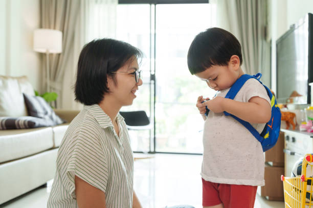 istock Asian Mother smiling while helping young boy adjust his blue backpack in a living room, preparing for school. 2180770307