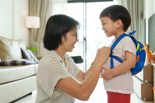 istock Asian Mother adjusts her young son backpack straps while smiling in a living room 2180770467