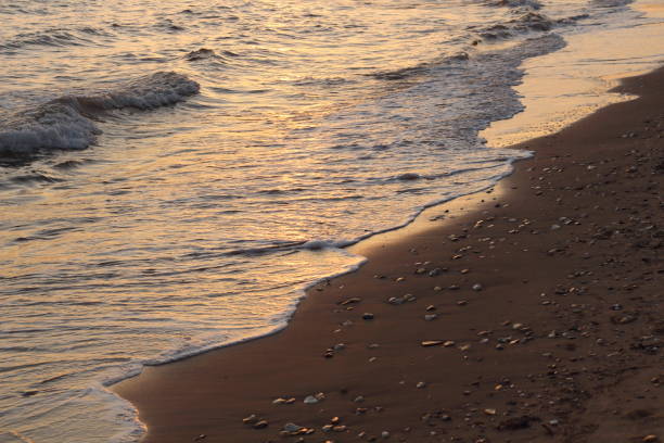The sunset casts a warm, golden glow on the sea and sand, creating a mesmerizing reflection that dances across the water's surface. As the vibrant hues of orange and pink blend with the tranquil blues