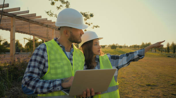 istock Caucasian colleagues engineers hardhat uniform male man holding laptop pc computer guy speak discussing data talking to female woman girl worker pointing finger showing gesture construction site park 2180776047