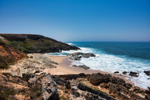istock Coastal landscape with rocky cliffs, sandy beach, and blue ocean waves under a clear sky. 2180777754