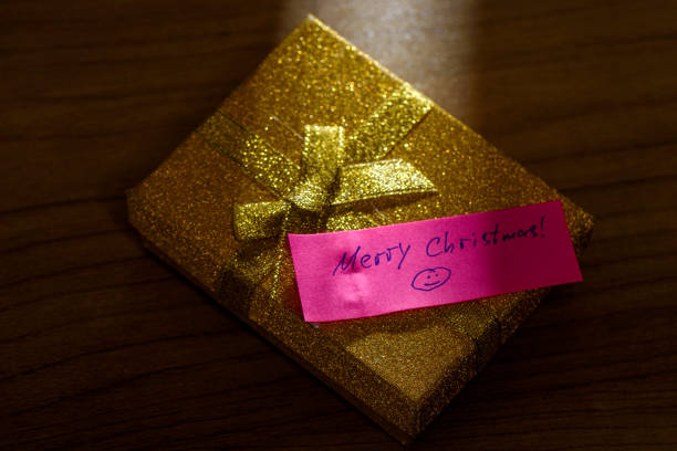 Golden gift box with handwritten note Merry Christmas under beam of light. Wooden background.