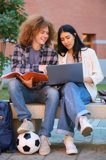 istock Two students collaborating on a project using laptop and textbook outdoors 2180783872