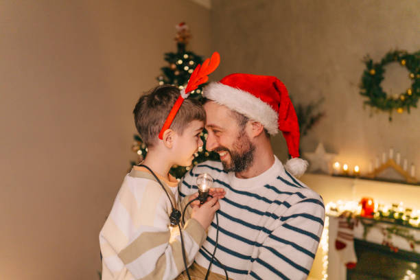 Photo of a father and son sharing a warm moment by the twinkling Christmas tree, with cozy decorations surrounding them as they prepare for the holiday.
