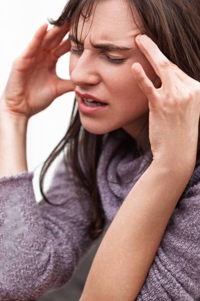Young woman touching her temples, trying to relieve a tension headache with a painful expression, showing signs of stress and suffering at home